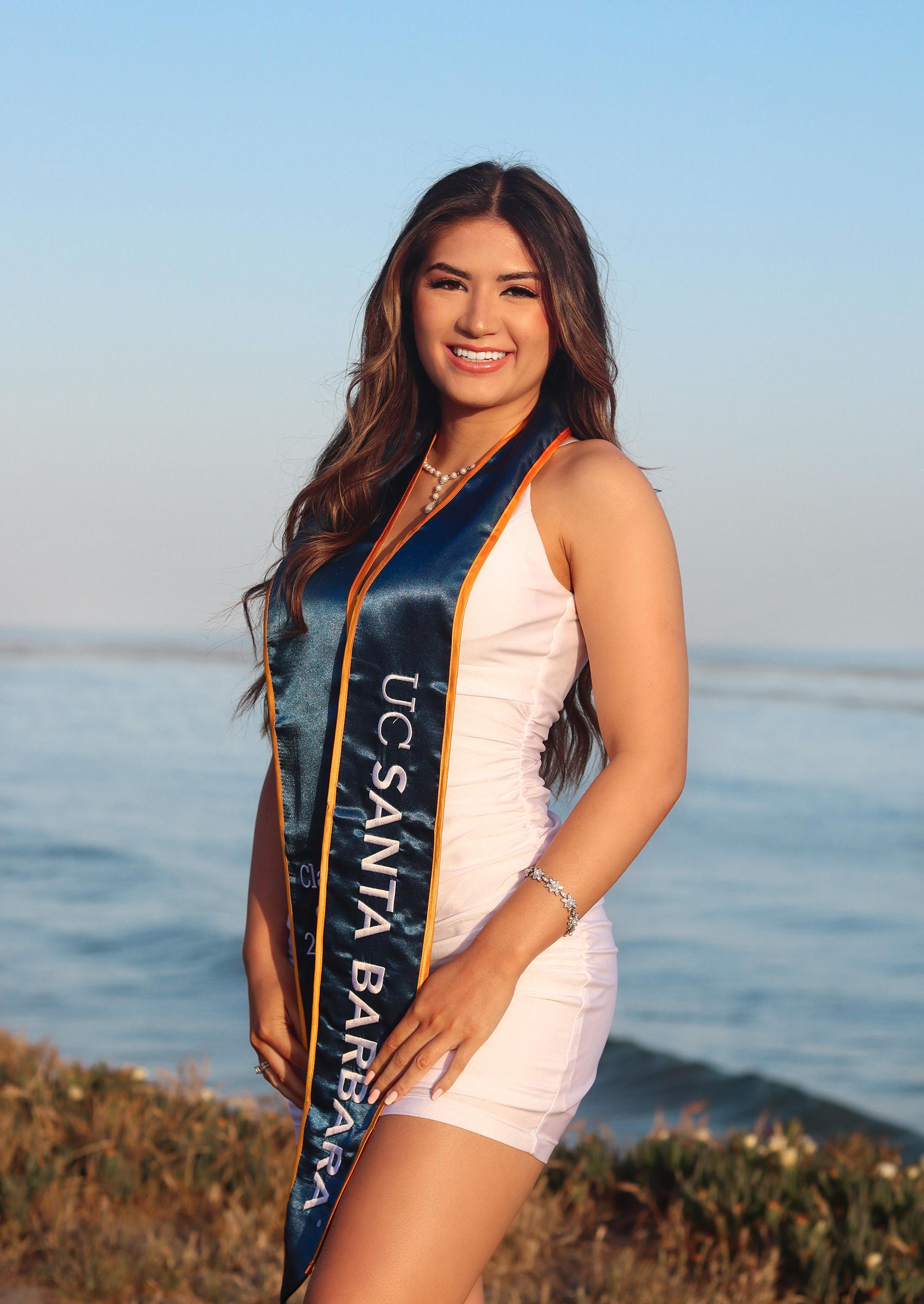 Dominique Mihaljevic wears a graduate stole on the bluffs at UC Santa Barbara with the ocean in the background