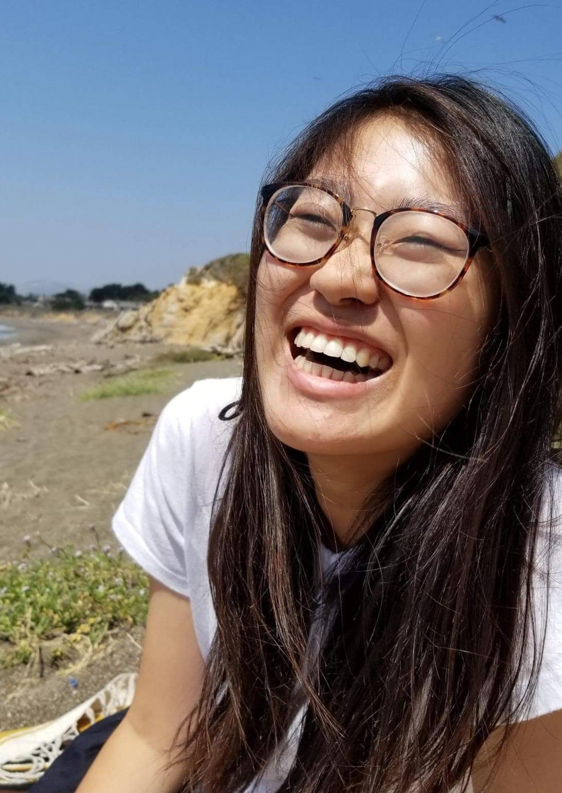 Michelle Chiu sits on the beach wearing glasses and laughing