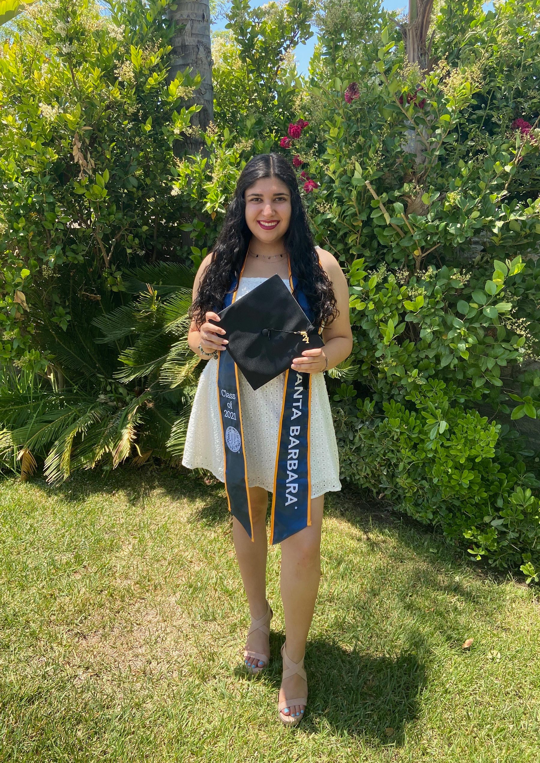 Shiva Areff stands in front of foliage wearing graduate attire