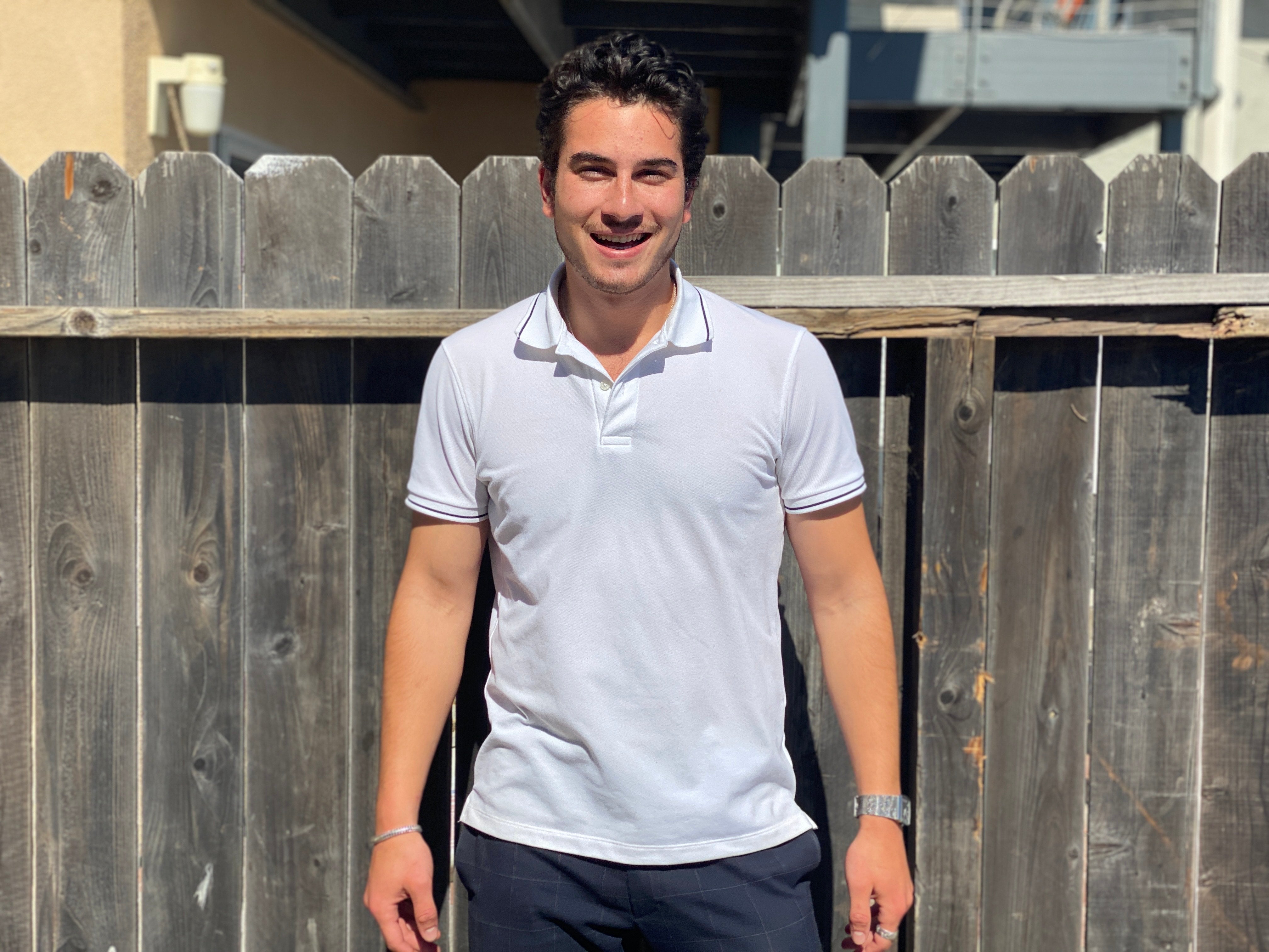 Student stands in front of a fence, an example of a plain background.