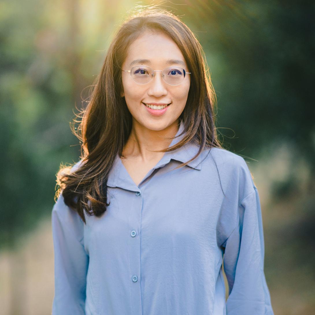 Murphy Niu wears a blue shirt in the forest with the sun behind her
