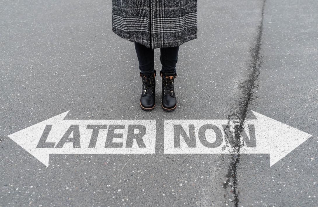 A person stands on concrete before two arrows, one says 'LATER' and the other says 'NOW'